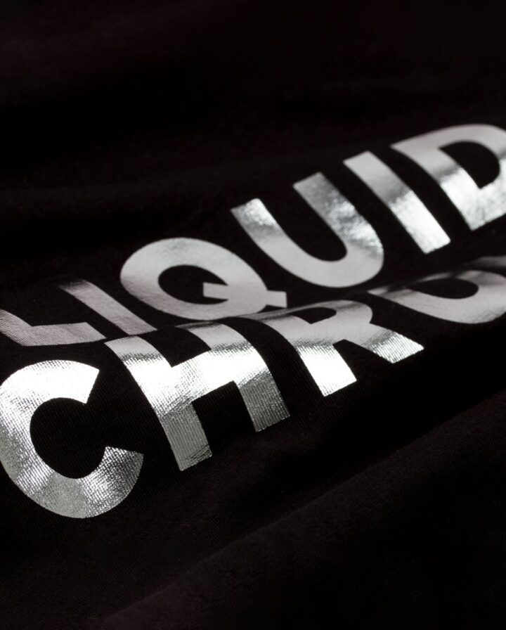 Nahaufnahme von Schrift als Front-Print in glänzender und reflektierender Chromeoptik auf einem schwarzen T-Shirt