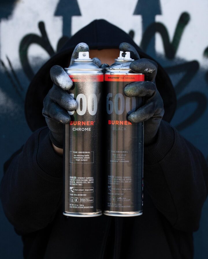 Mann hält zwei Spraydosen in Chrome und Schwarz vor seinem Gesicht frontal in die Kamera