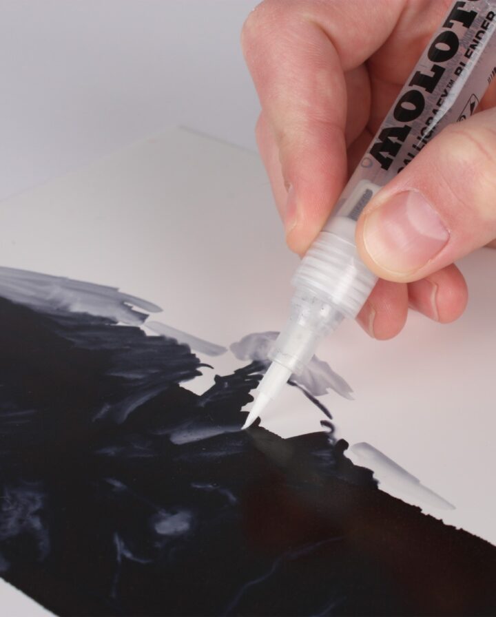 Hand hält transparentem Marker mit Pinselspitze auf eine schwarz angemalte Fläche Papier