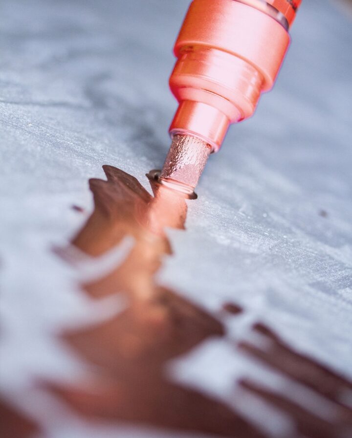 glänzende Kupferfarbe aus einem Stift auf einem grauen Untergrund im Closeup